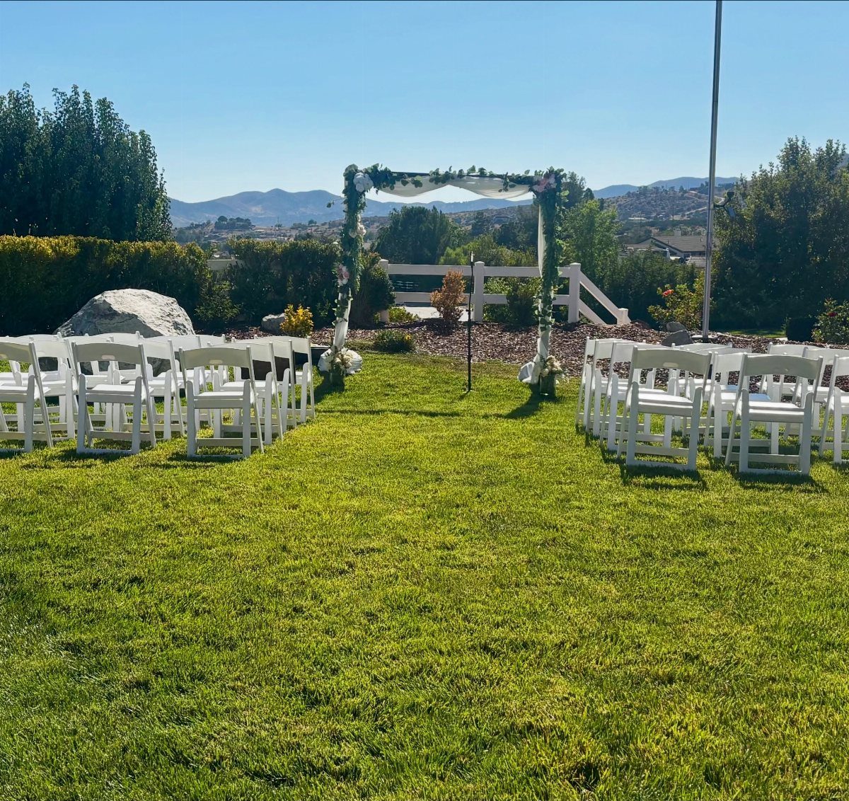 White folding chairs and a floral arch set up on a green lawn.