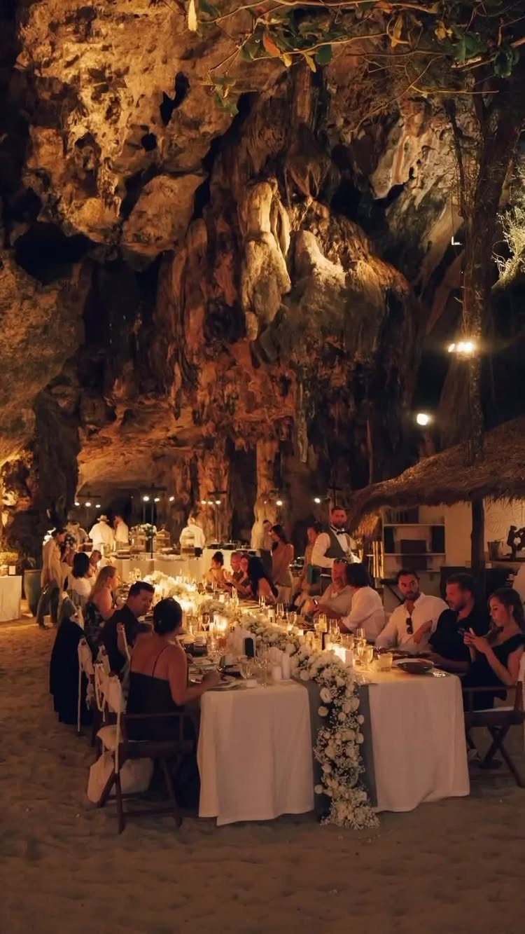 Wedding banquet table with white flowers set inside a large, illuminated rocky cave.