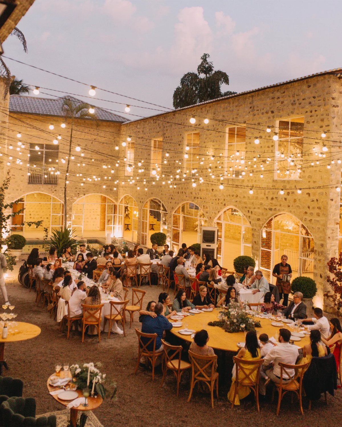 Outdoor wedding reception in a stone courtyard with string lights and wooden tables.