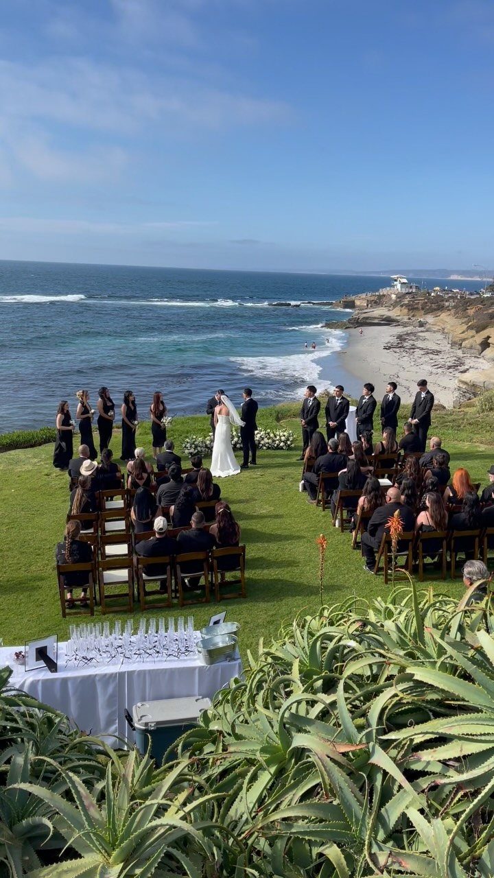 Wedding ceremony on a grassy cliff overlooking the ocean with guests in chairs.
