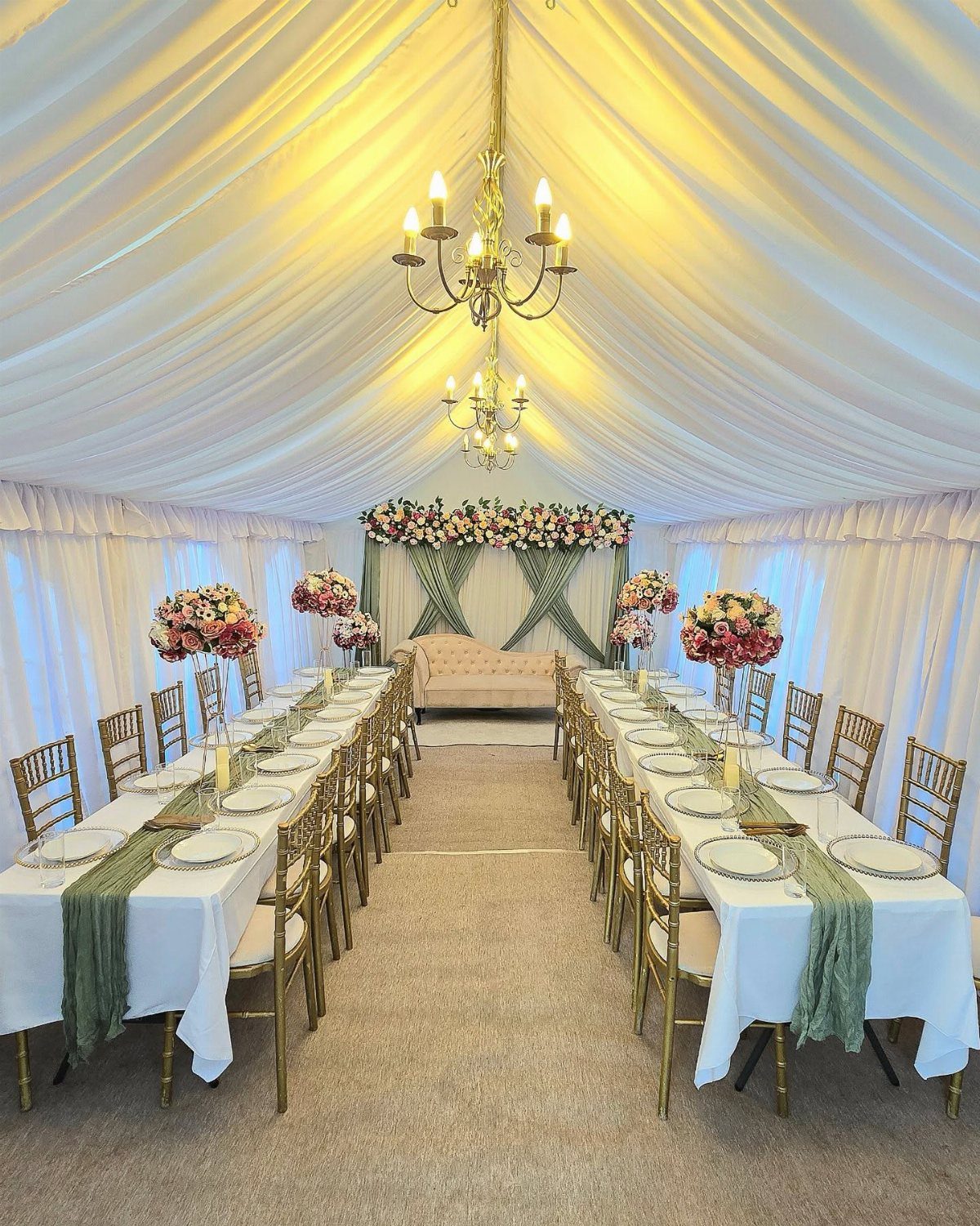 Wedding reception setup with gold Chiavari chairs and chandeliers under a white tent.