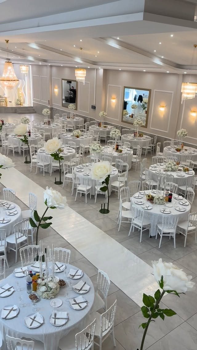 Wedding reception hall with white round tables, chairs, and floral centerpieces and aisle runner.