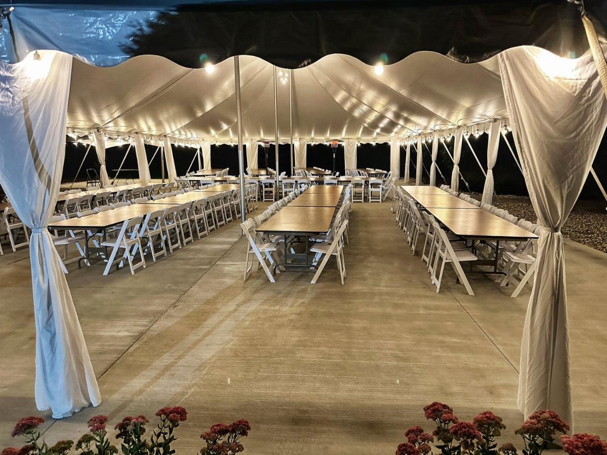 White event tent with long tables, folding chairs, and warm overhead lighting.