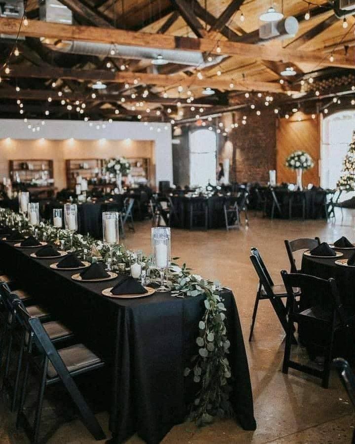 Black wedding reception tables with gold plates and greenery in a rustic hall