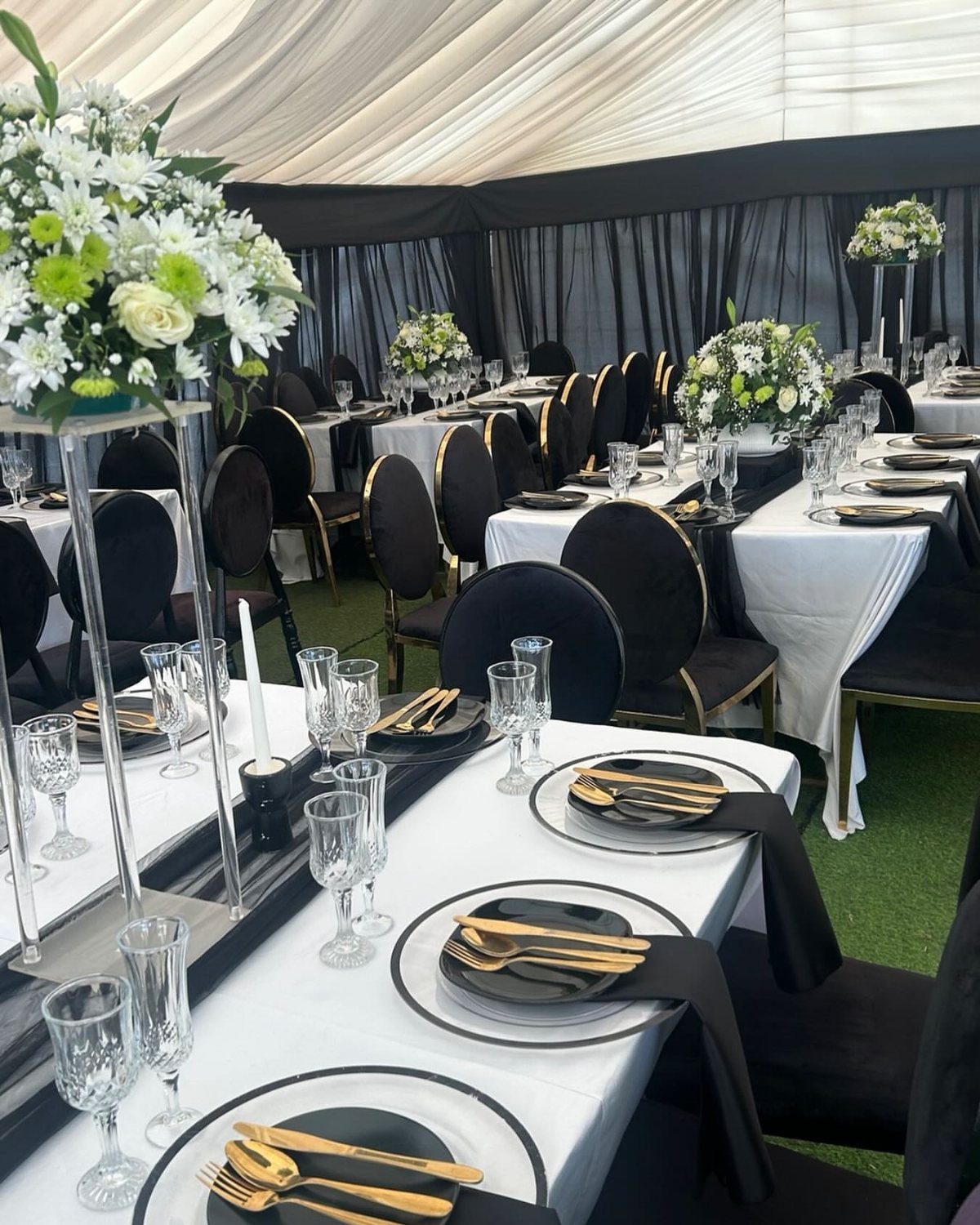 Wedding tables with white cloths, black plates, gold cutlery, and black chairs.