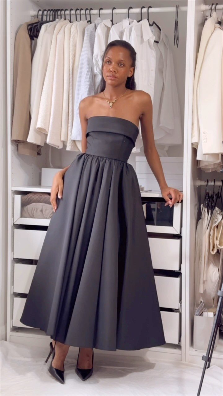 Woman in a strapless black gown posing in a white walk-in closet.