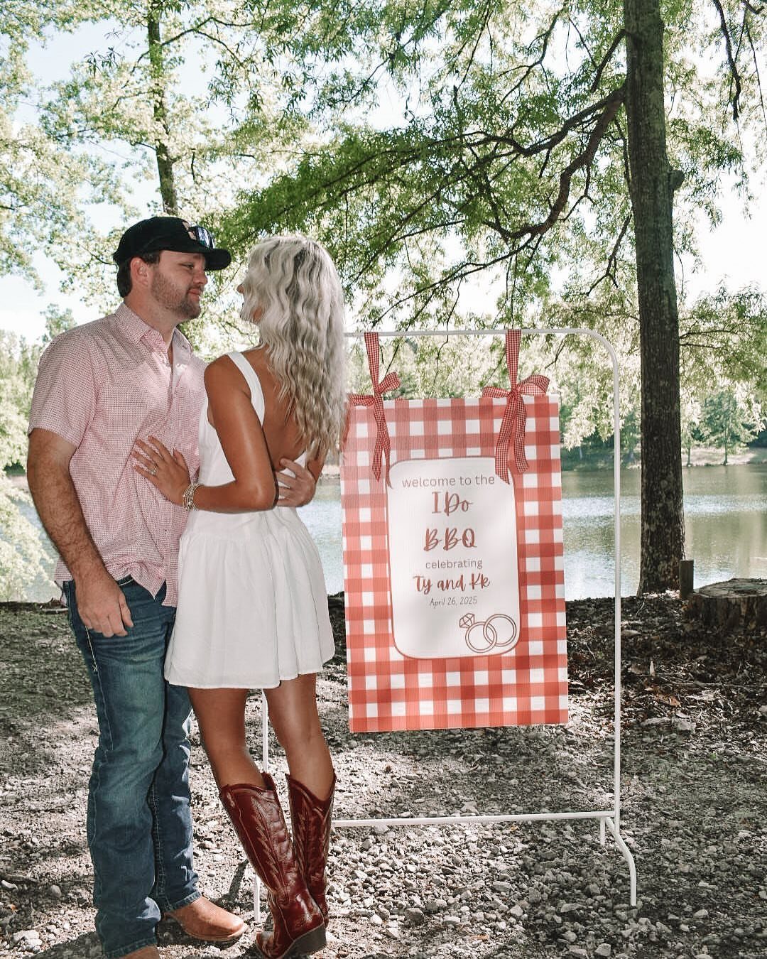 Couple standing by a red checkered BBQ welcome sign near a river