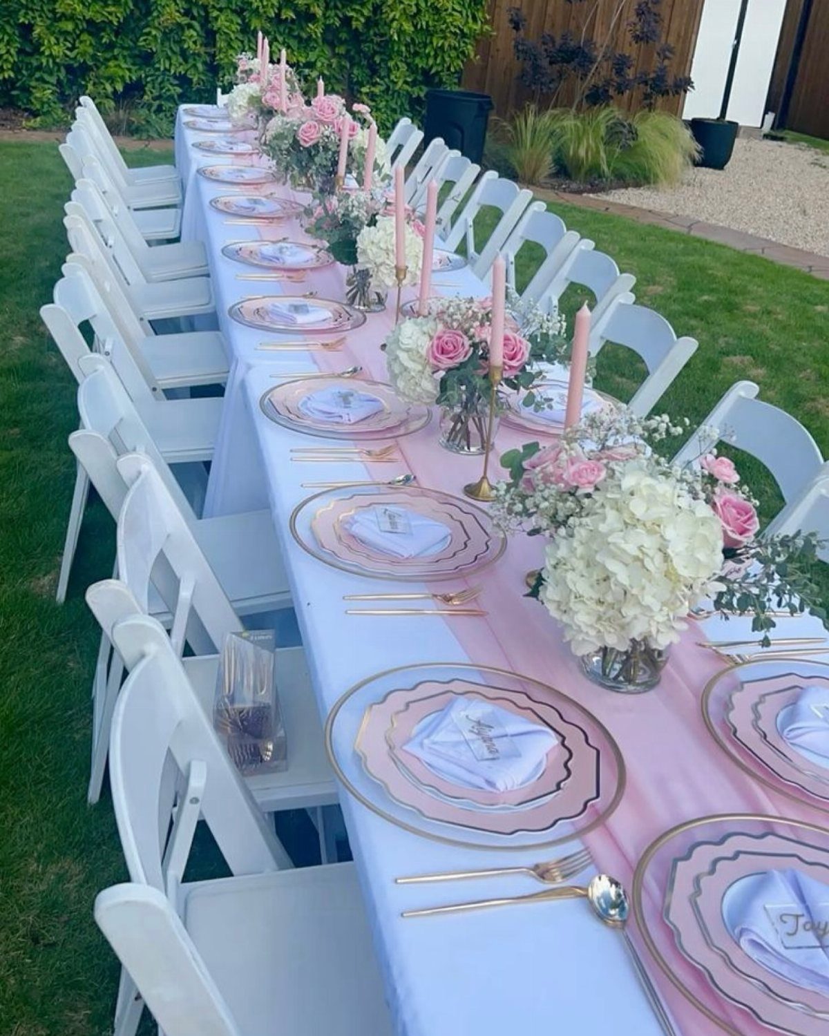 Floral centerpieces with pink and white roses on a long outdoor party table.