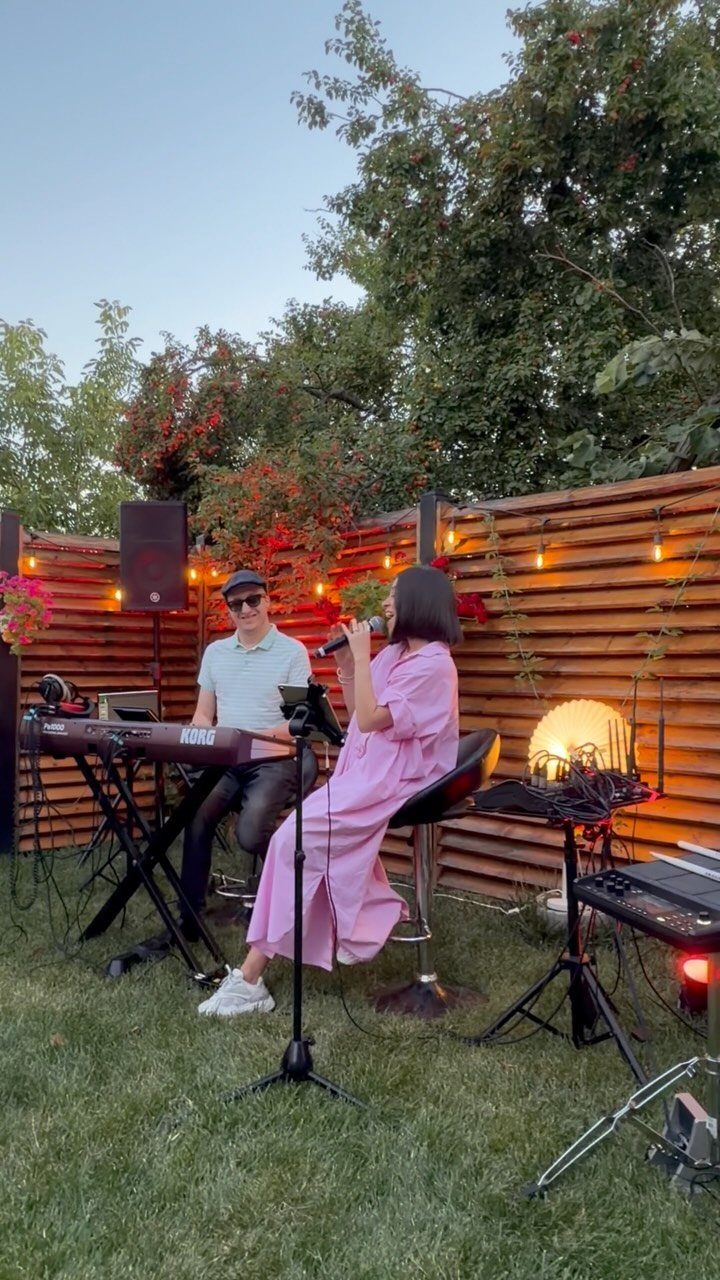 Musicians performing live music in a backyard with string lights and a wooden fence.