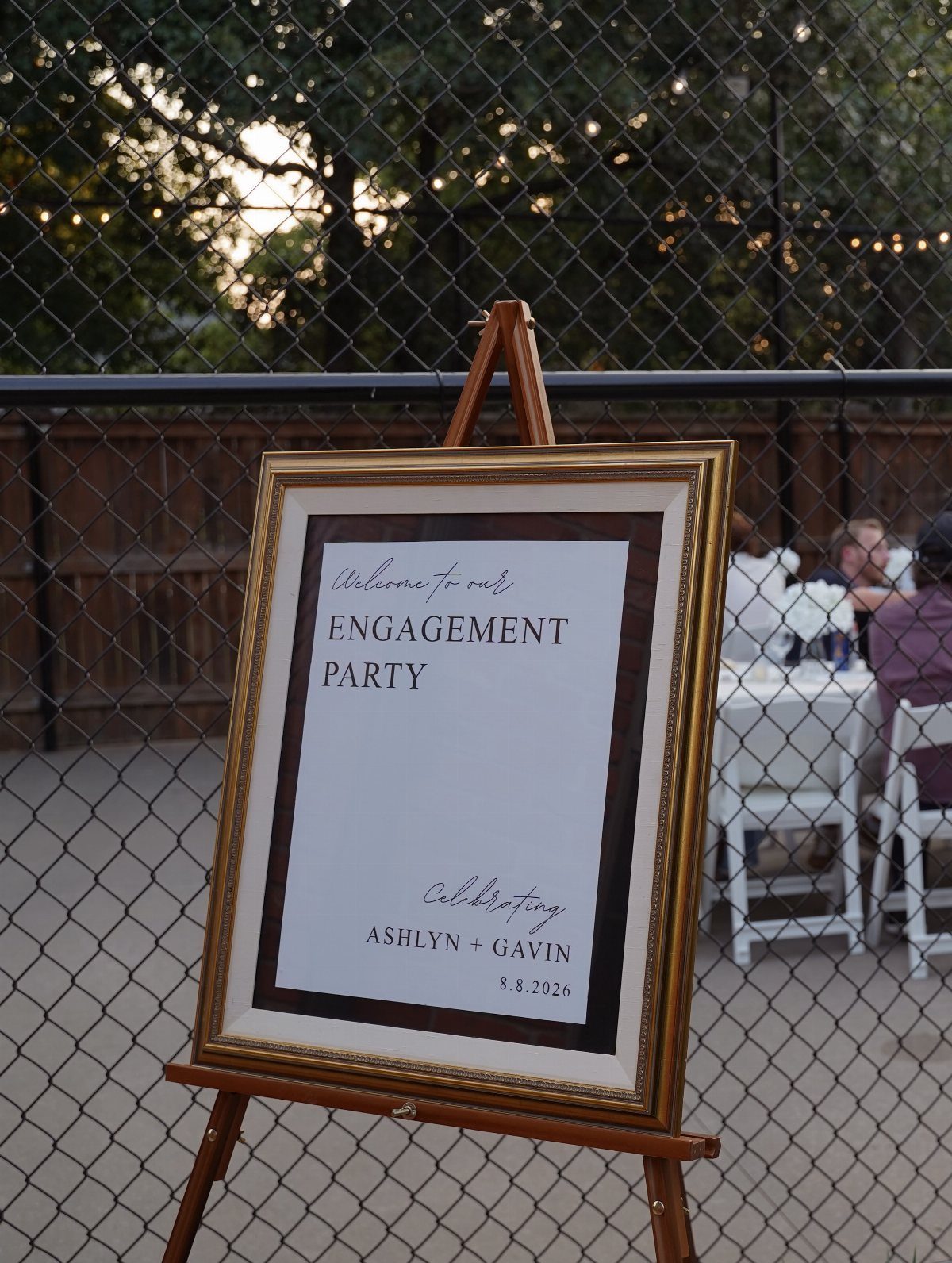 Framed engagement party welcome sign on a wooden easel in an outdoor setting