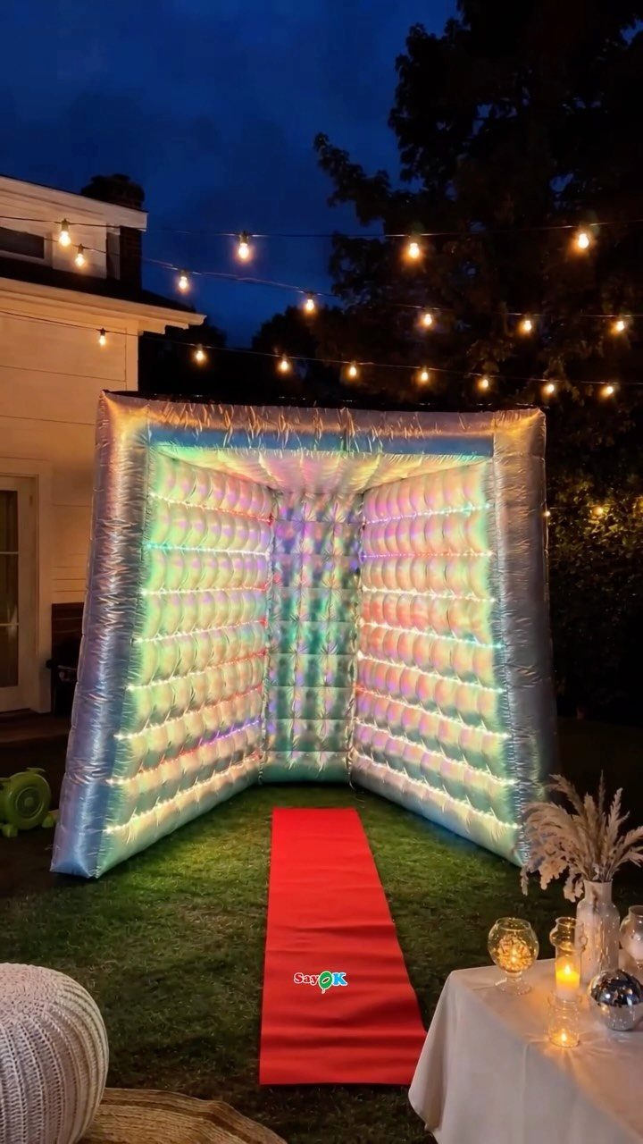 Inflatable iridescent silver photo booth with a red carpet on a grassy lawn.