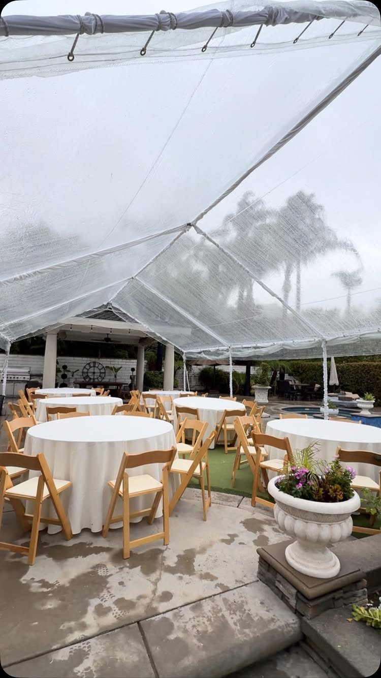 White event tent covering round tables and wooden chairs on an outdoor patio.