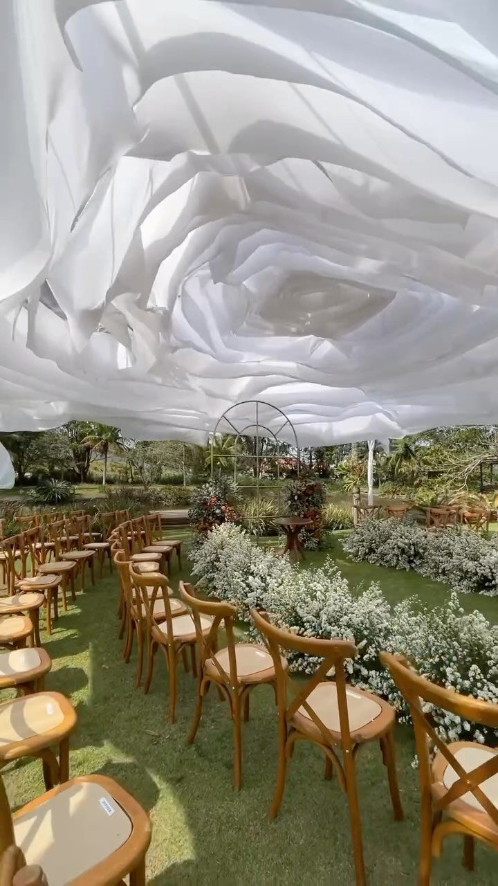 White draped fabric canopy over wooden chairs and floral arch in a garden