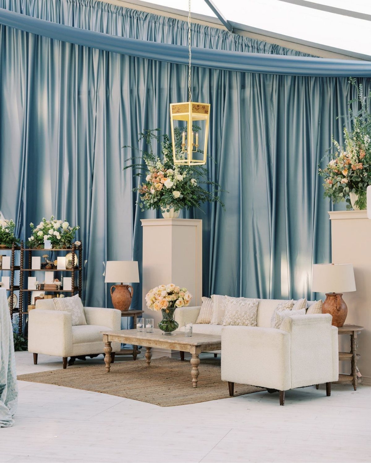 Blue draped tent sidewalls surrounding a white lounge area with floral arrangements.