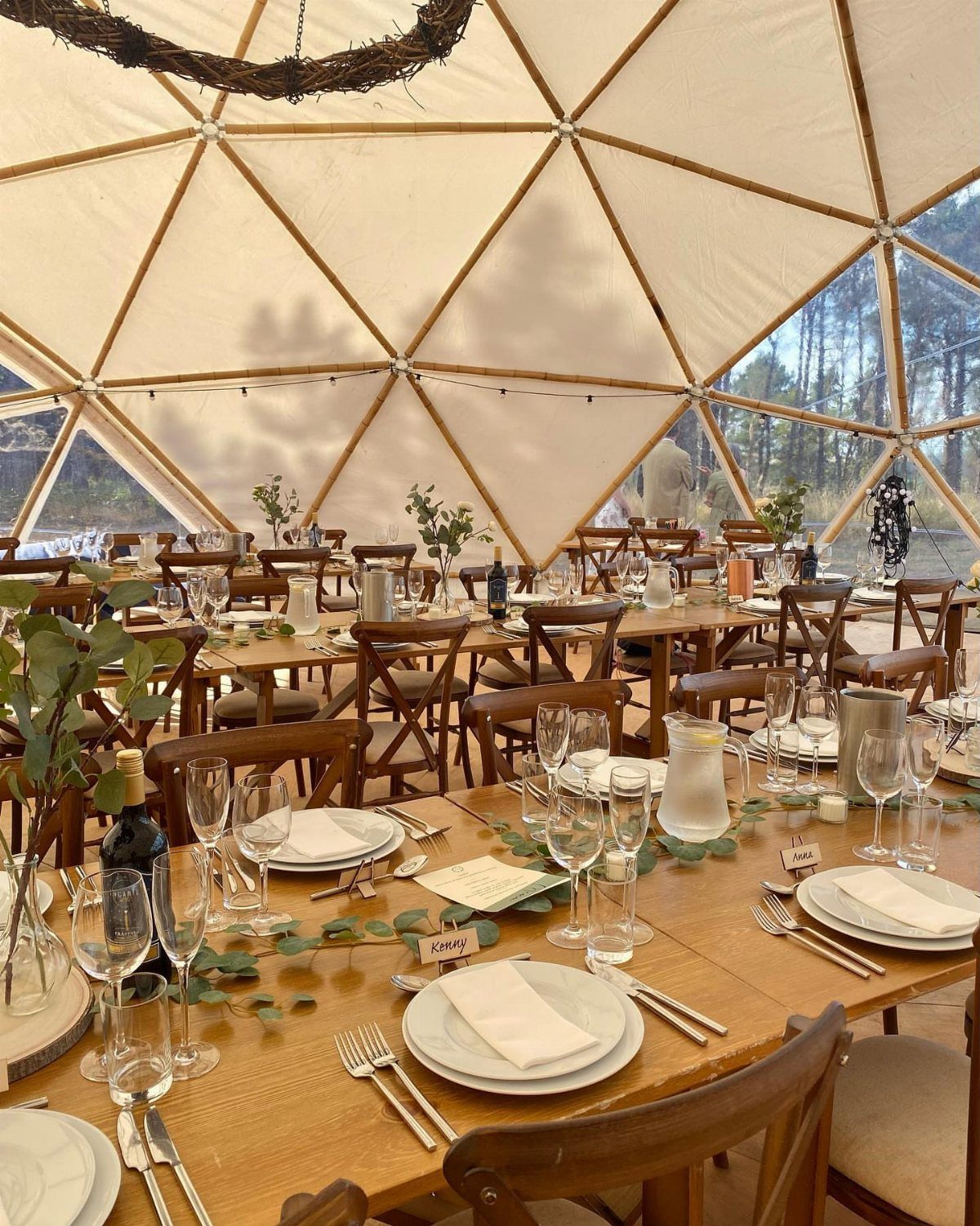 Geodesic dome tent wedding setup with wooden tables, white linens, and greenery runners.