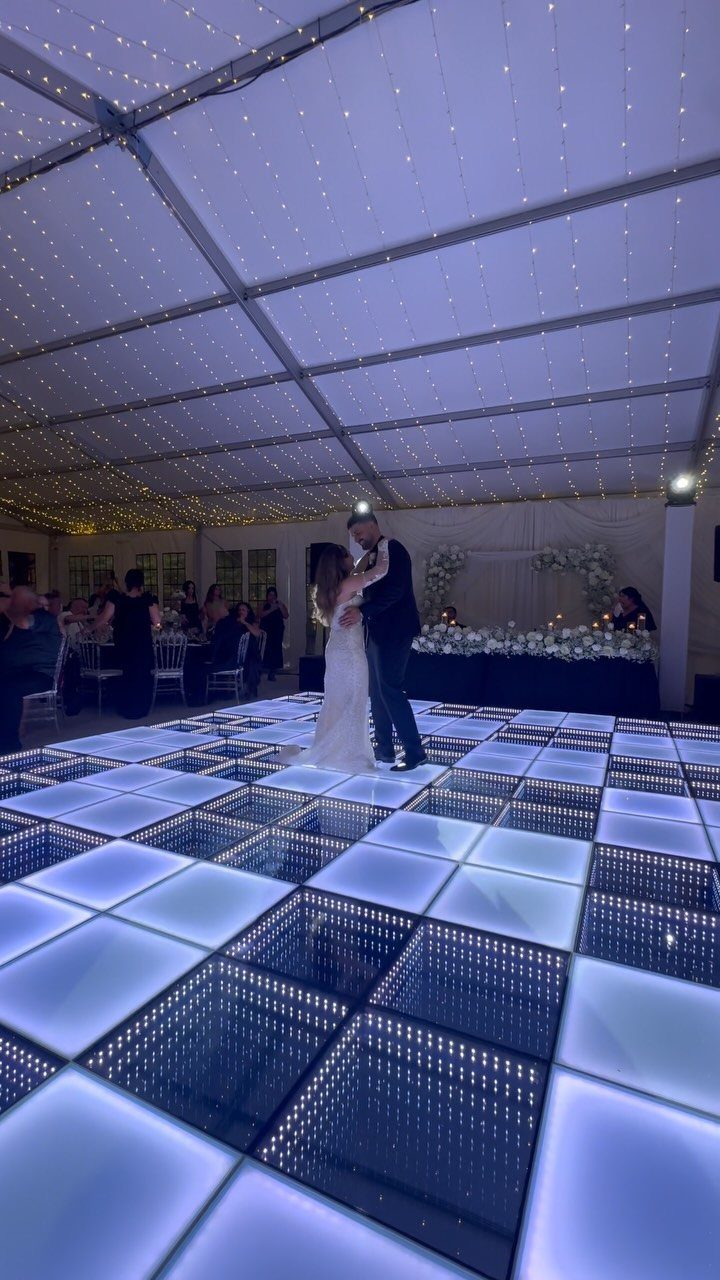 Couple dancing on a white LED dance floor inside a tent with string lights