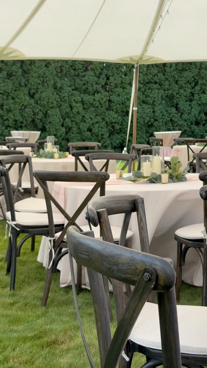 Cream sailcloth tent canopy over wedding tables with wooden cross-back chairs on grass