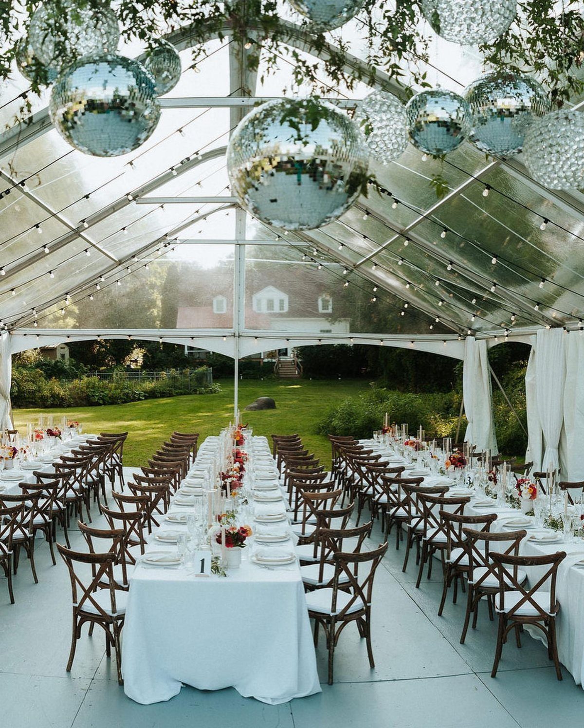 Long banquet tables with white linens and floral centerpieces under a clear tent.