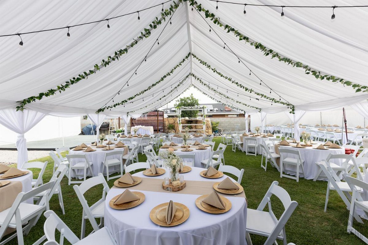 White event tent on a lawn with decorated round tables and string lights.