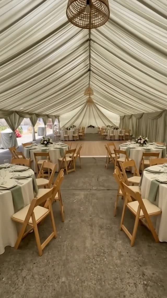 White draped marquee tent interior with round dining tables and wooden folding chairs.