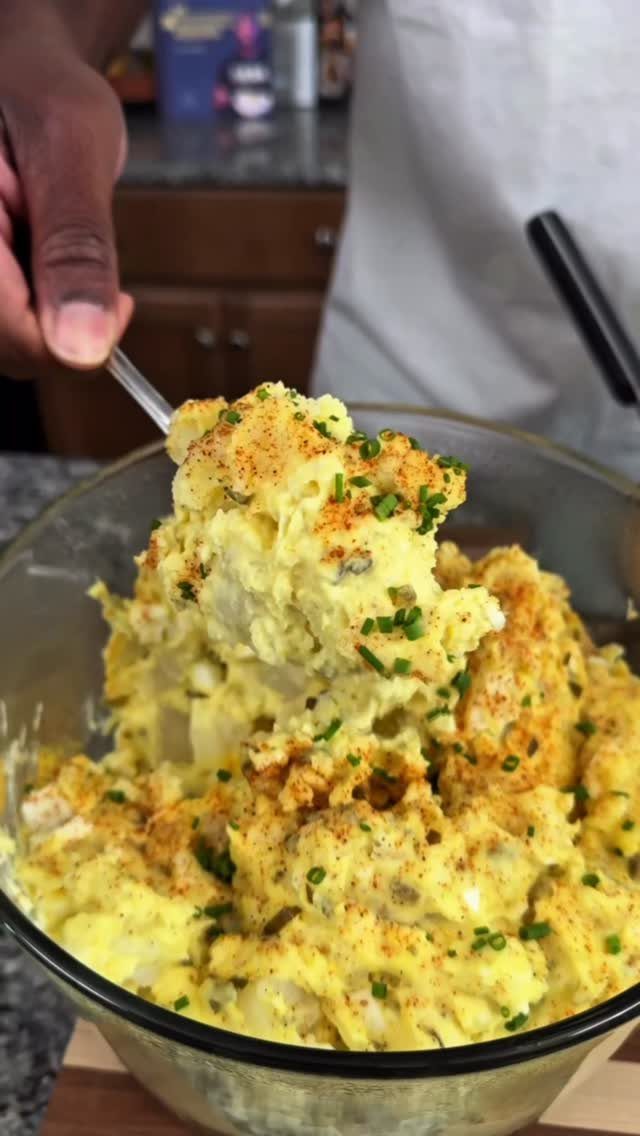Potato salad with paprika and chives being scooped from a glass bowl.