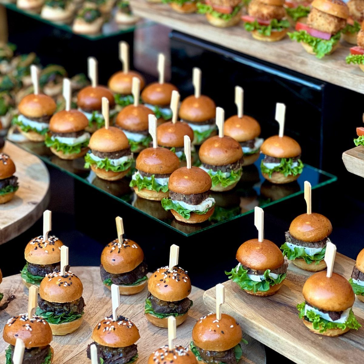 Mini beef sliders with lettuce and sauce on wooden and glass platters.