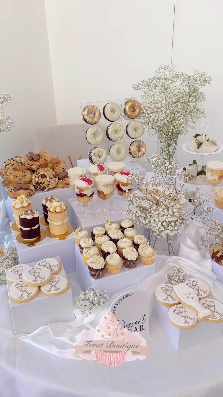 Dessert bar with cupcakes, cookies, and mini cakes decorated with white flowers.