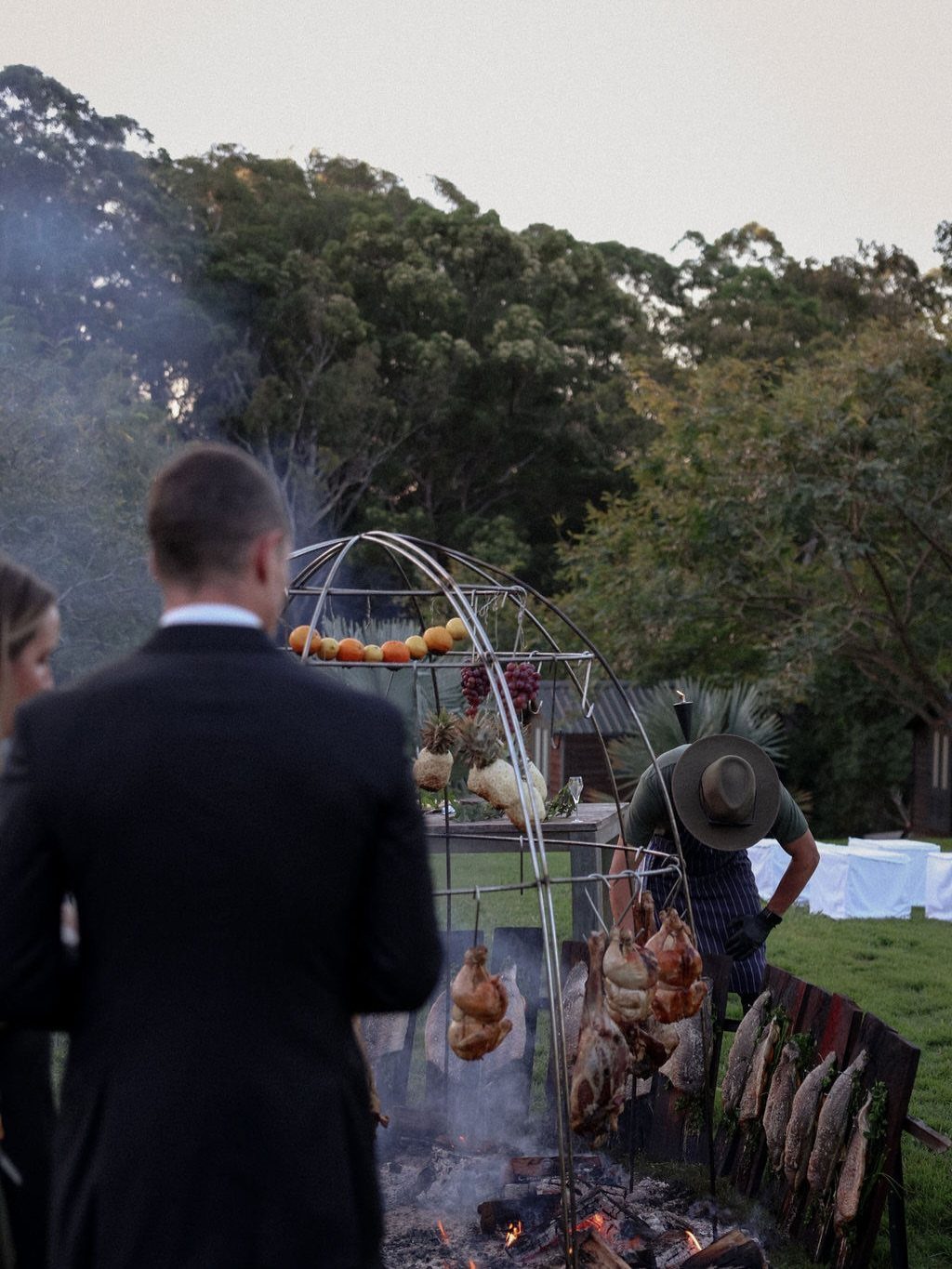 Chef cooking chickens and fish over open fire at outdoor wedding reception