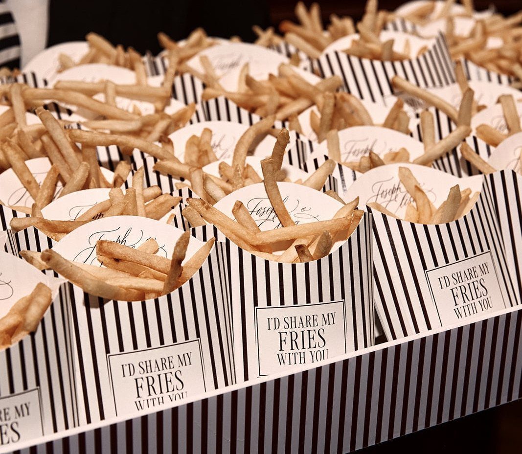 French fries in striped paper cones with labels on a striped table.