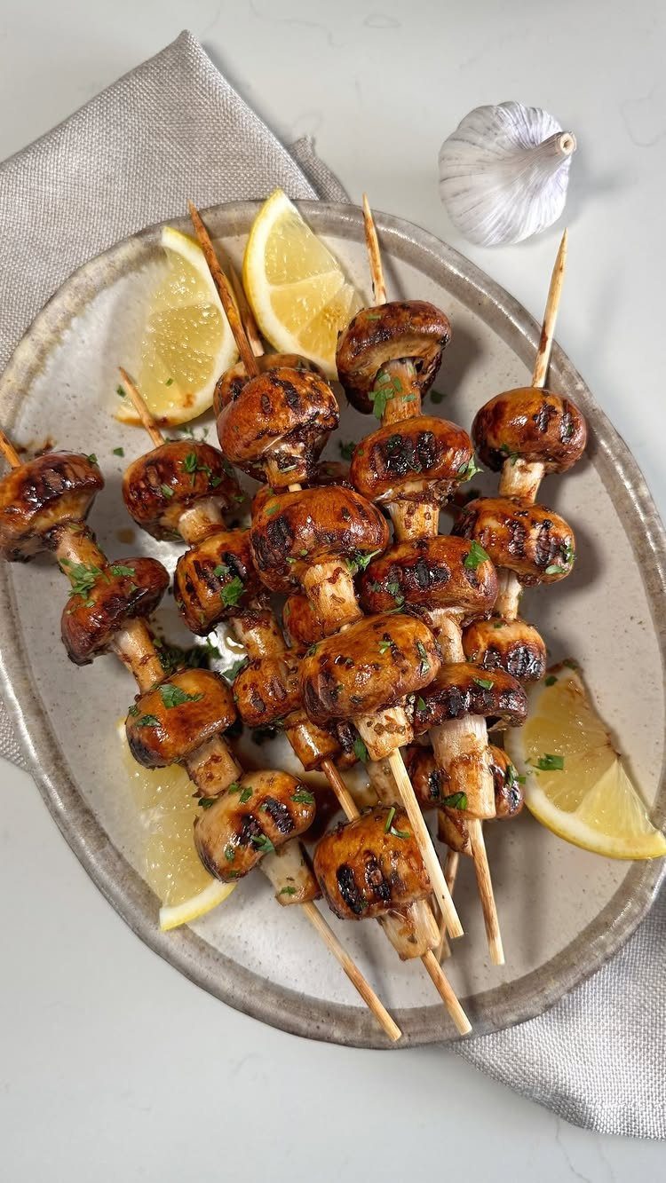 Grilled mushroom skewers with lemon wedges on a light oval platter.