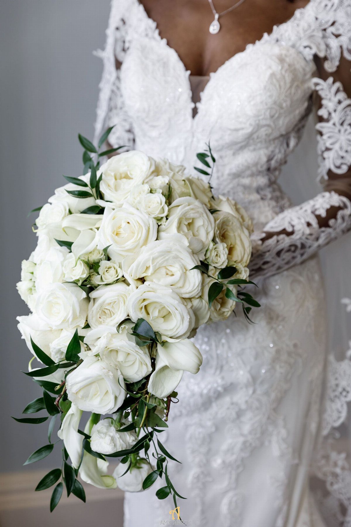 Cascading bouquet of white roses held by a bride in a lace gown.
