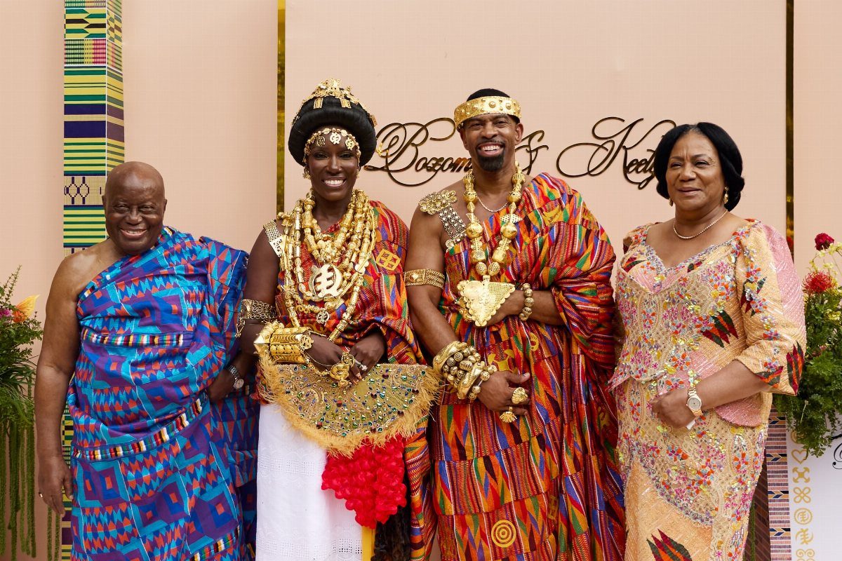Couple in traditional African Kente cloth and gold jewelry posing with family members.