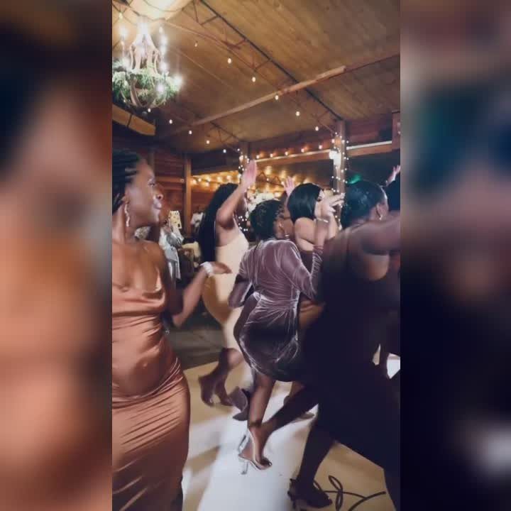 Black women in formal dresses dancing at a wedding reception in a rustic venue