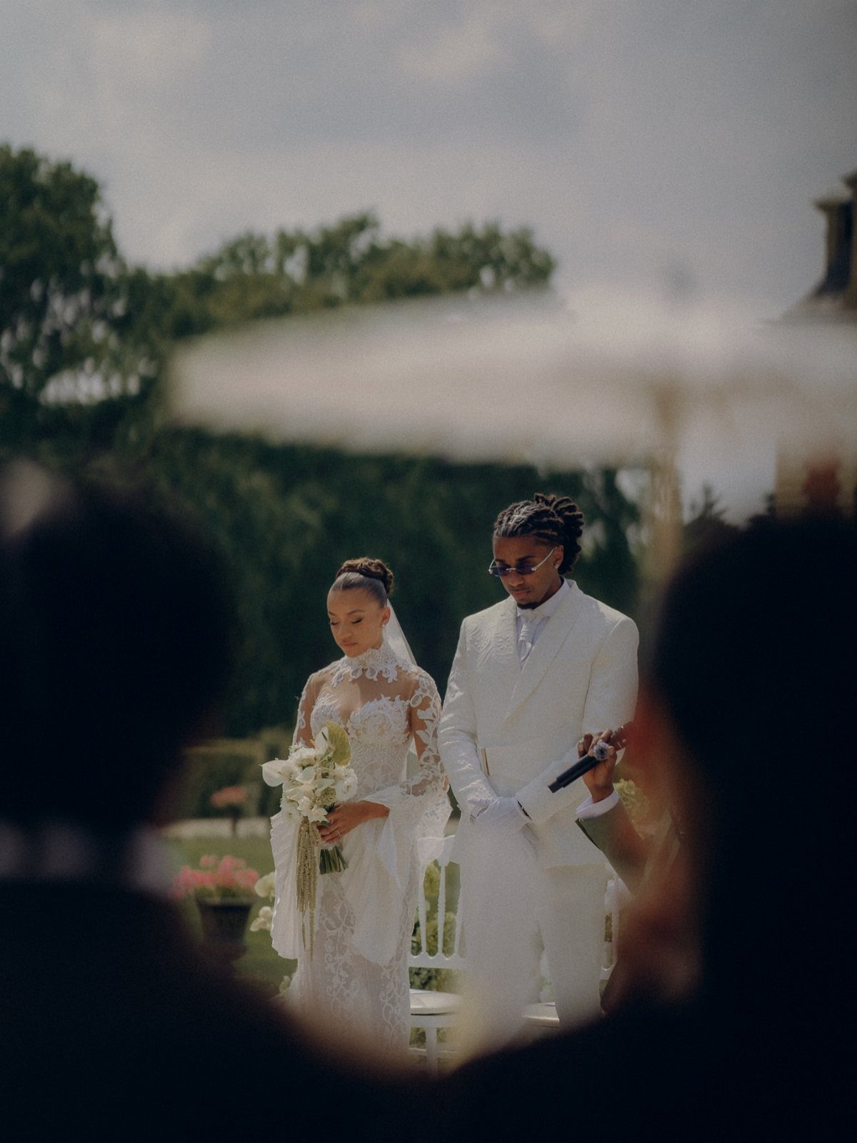 Black bride in lace gown and groom in white suit during outdoor wedding