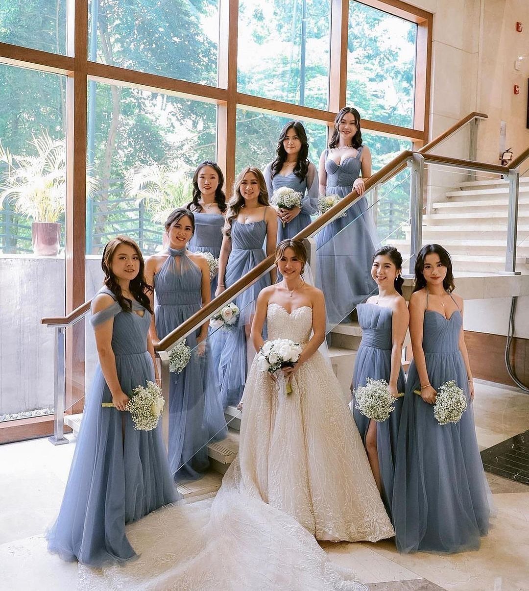 Bride in white gown with bridesmaids wearing dusty blue dresses on a staircase.