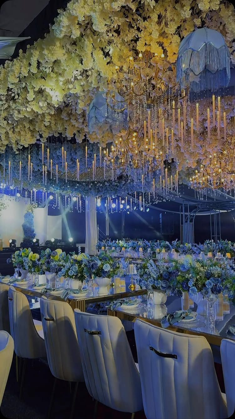 Wedding reception tables with blue flowers under a ceiling of yellow autumn foliage.