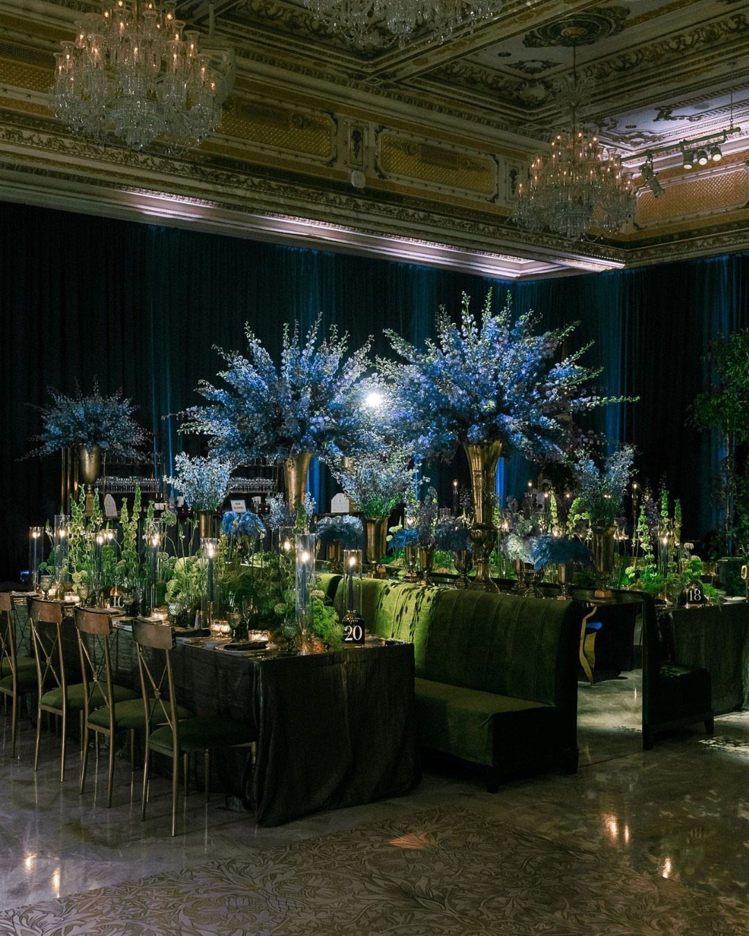 Blue floral centerpieces on emerald green velvet tables in a luxury ballroom.