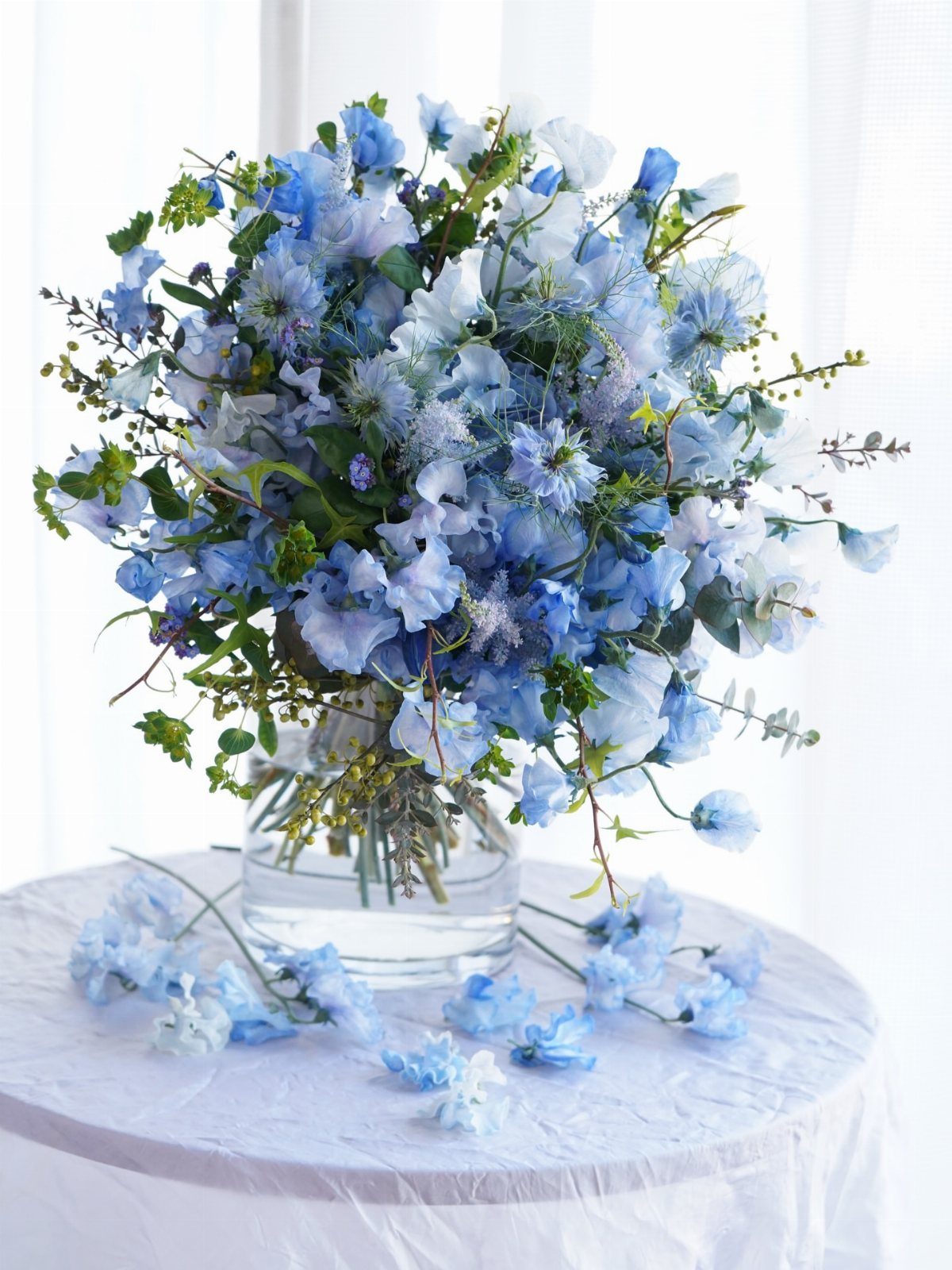 Dusty blue floral arrangement in a glass vase on a white table.