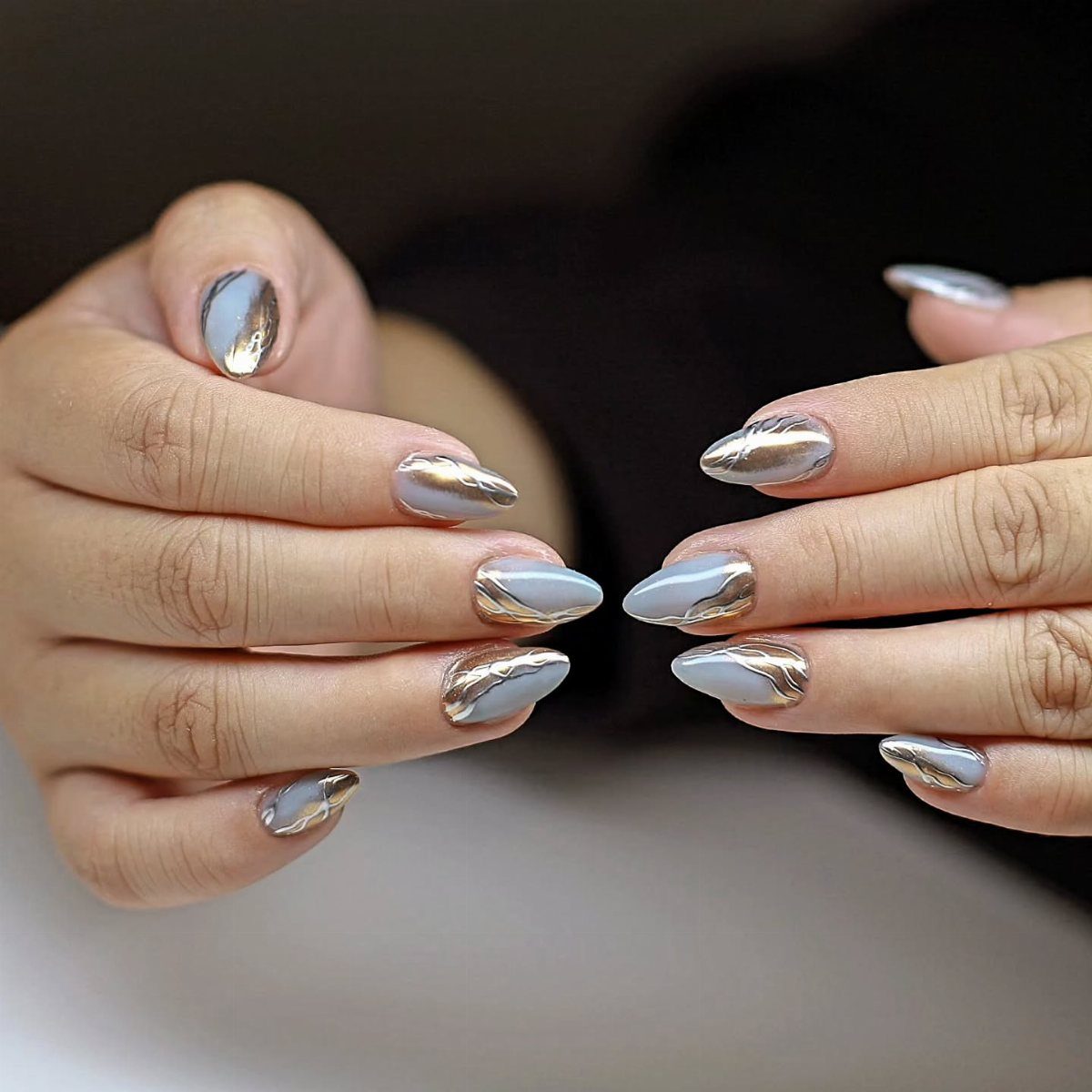 Dusty blue nails with metallic gold and copper swirling accents on almond-shaped tips.