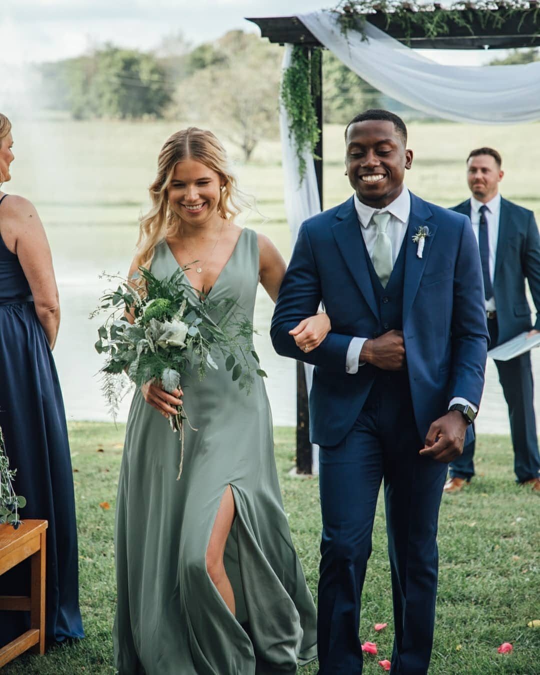 Smiling couple walking arm-in-arm, woman in sage green dress, man in navy suit.