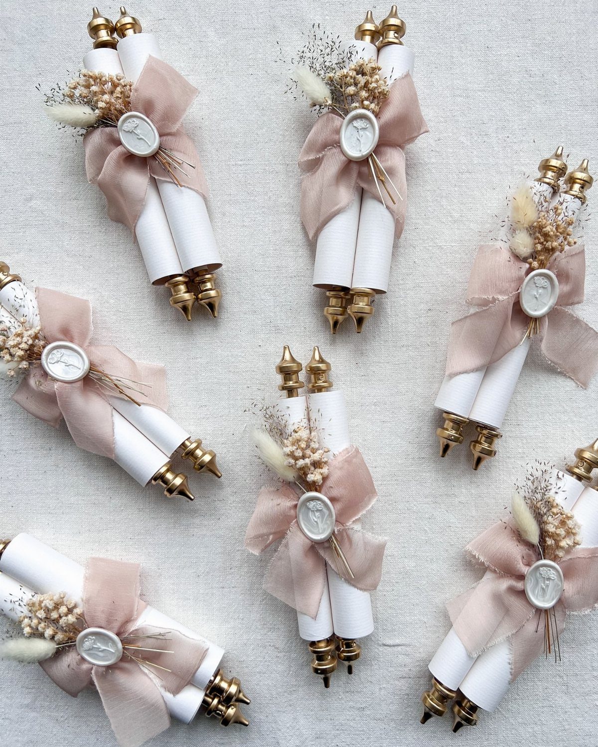 Rolled white wedding scrolls tied with rose ribbons and dried pampas grass florals.