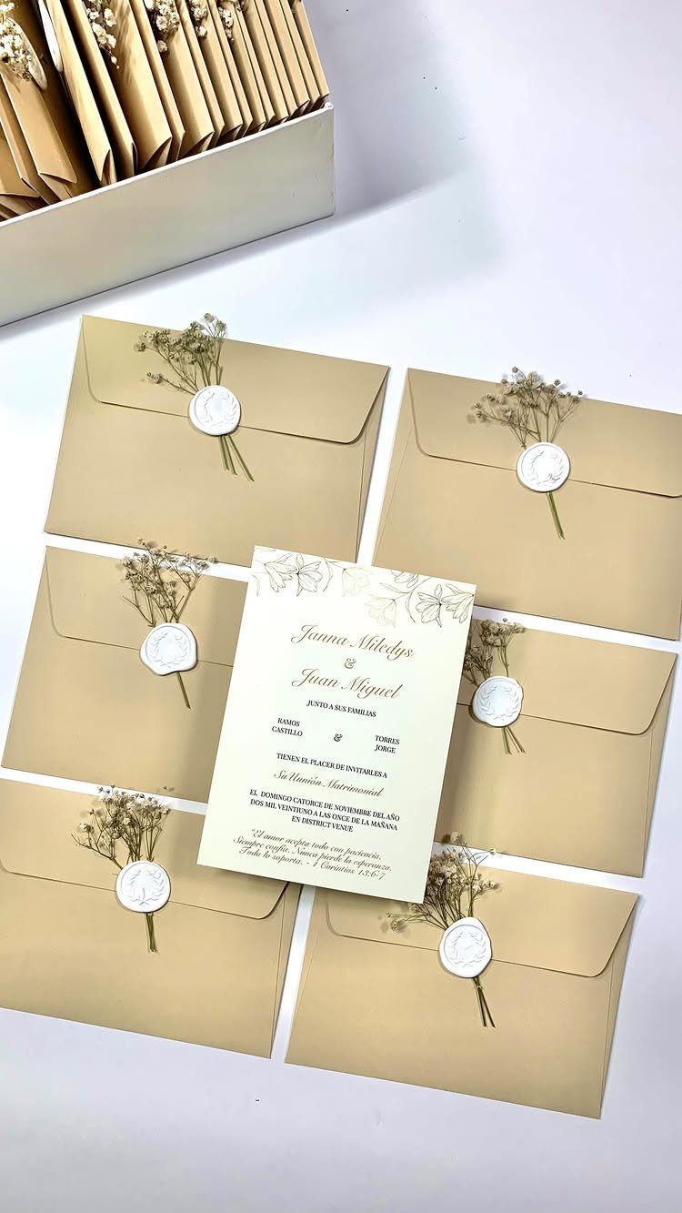 Brown kraft envelopes with white wax seals and dried flowers beside a wedding invitation.