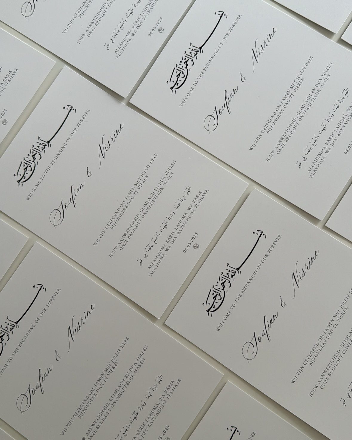White wedding invitation cards featuring elegant black cursive calligraphy and Arabic script.