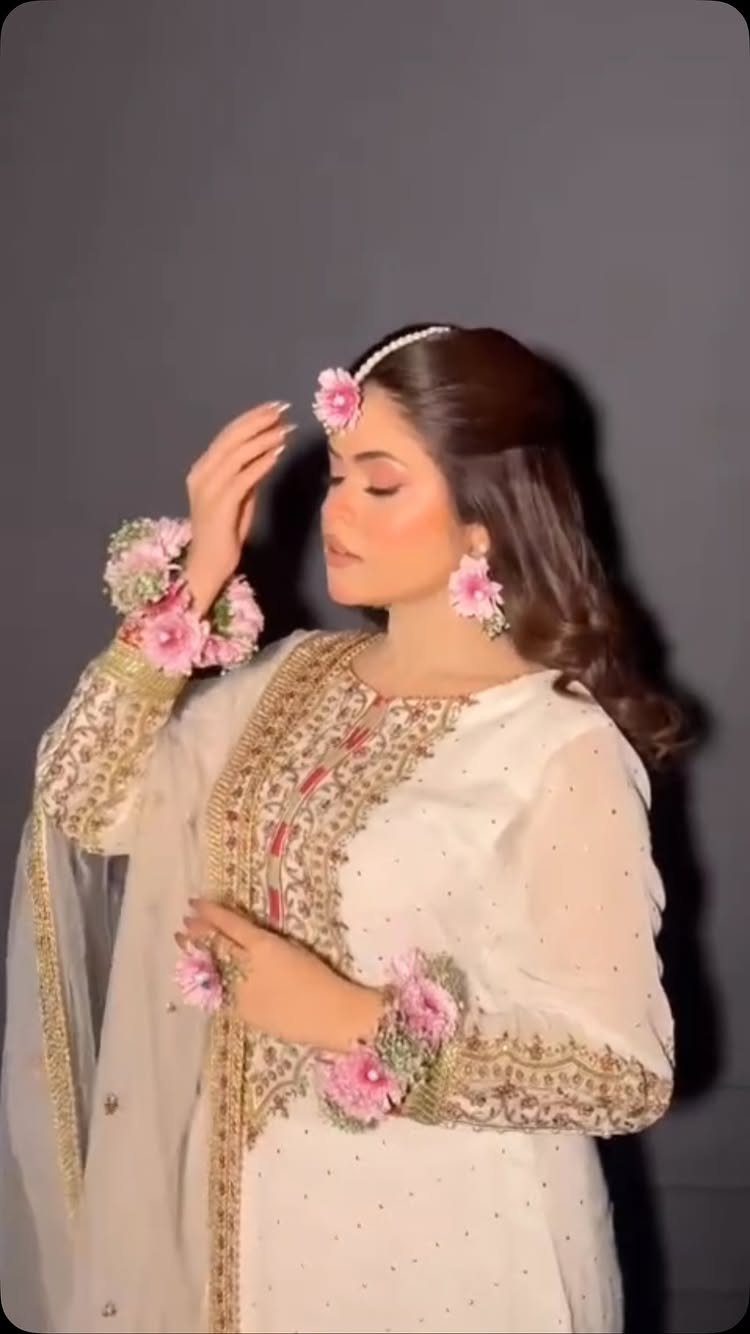 Woman wearing a white embroidered outfit and pink floral bridal maang tikka jewelry.