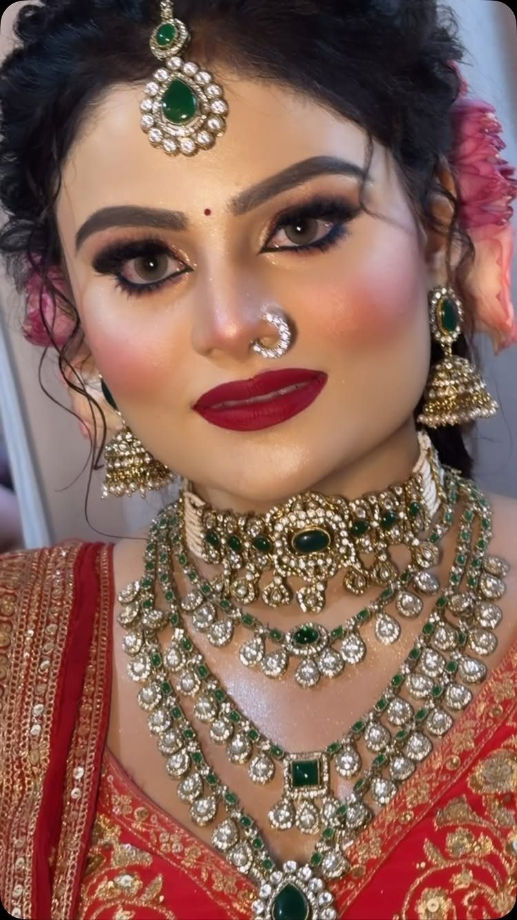 Woman wearing heavy gold and emerald jhumka earrings with a slim maang tikka