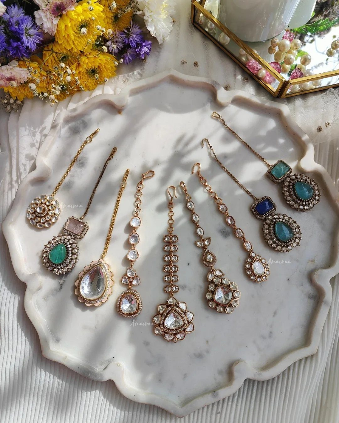 Various gold maang tikka jewelry pieces with gemstones on a white marble tray