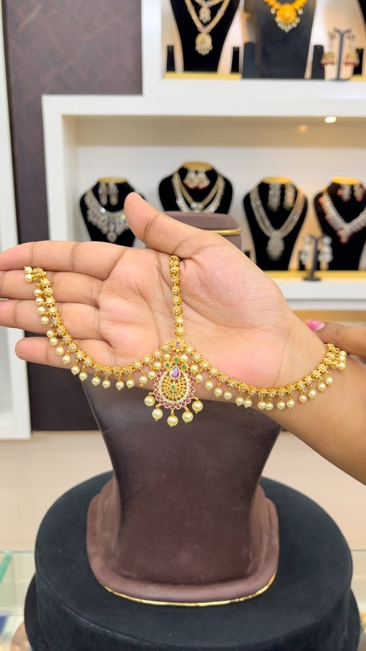 Gold bridal maang tikka with pearls and gemstones held in a hand