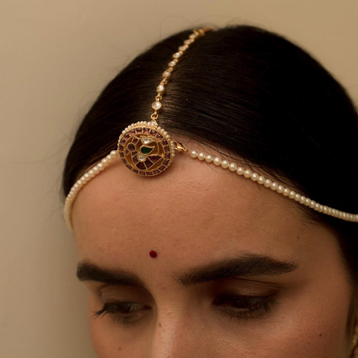 Woman wearing a gold and pearl bridal maang tikka with a red bindi.