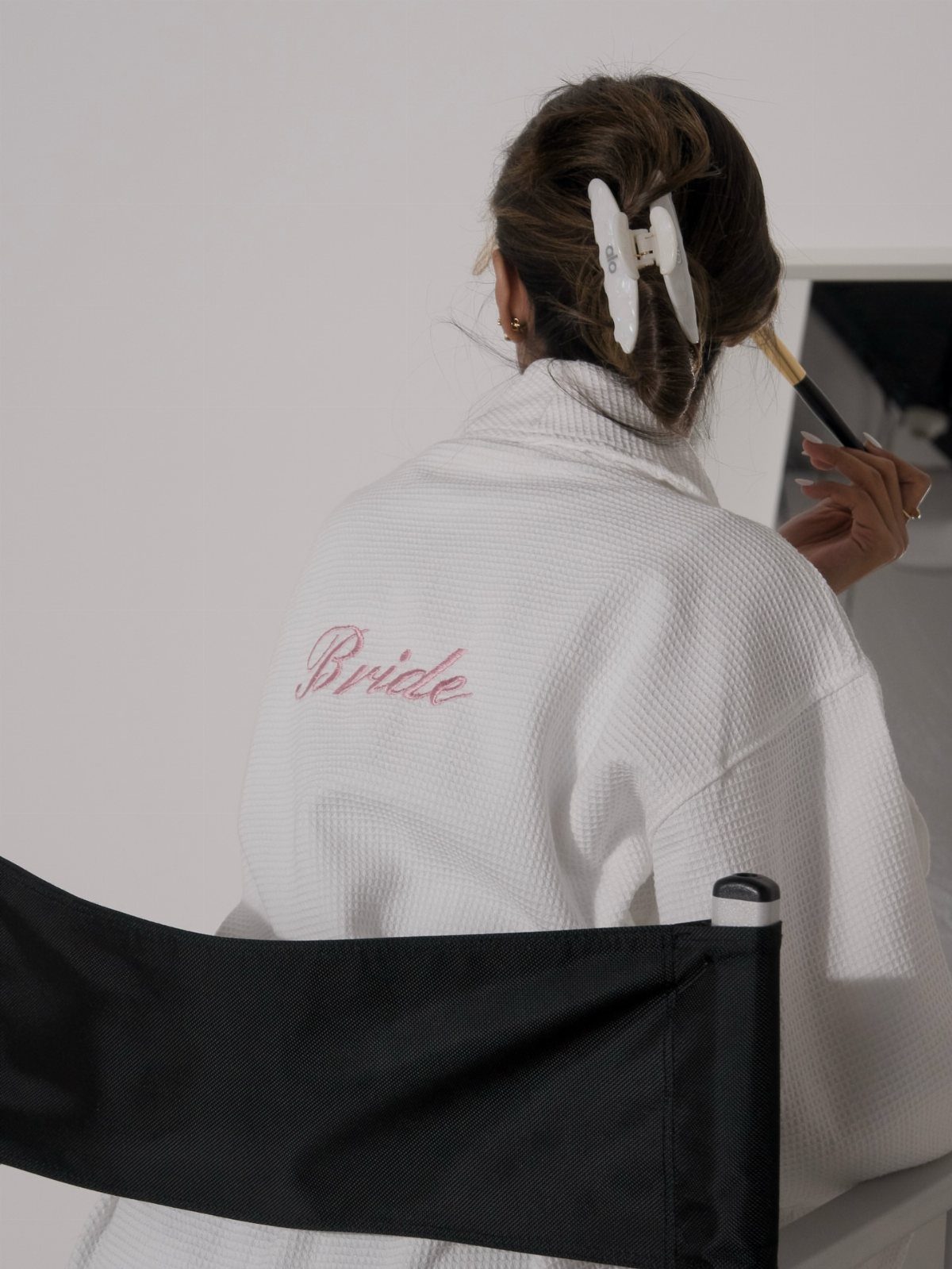Woman in a white waffle-knit bridal robe getting her makeup done from behind.