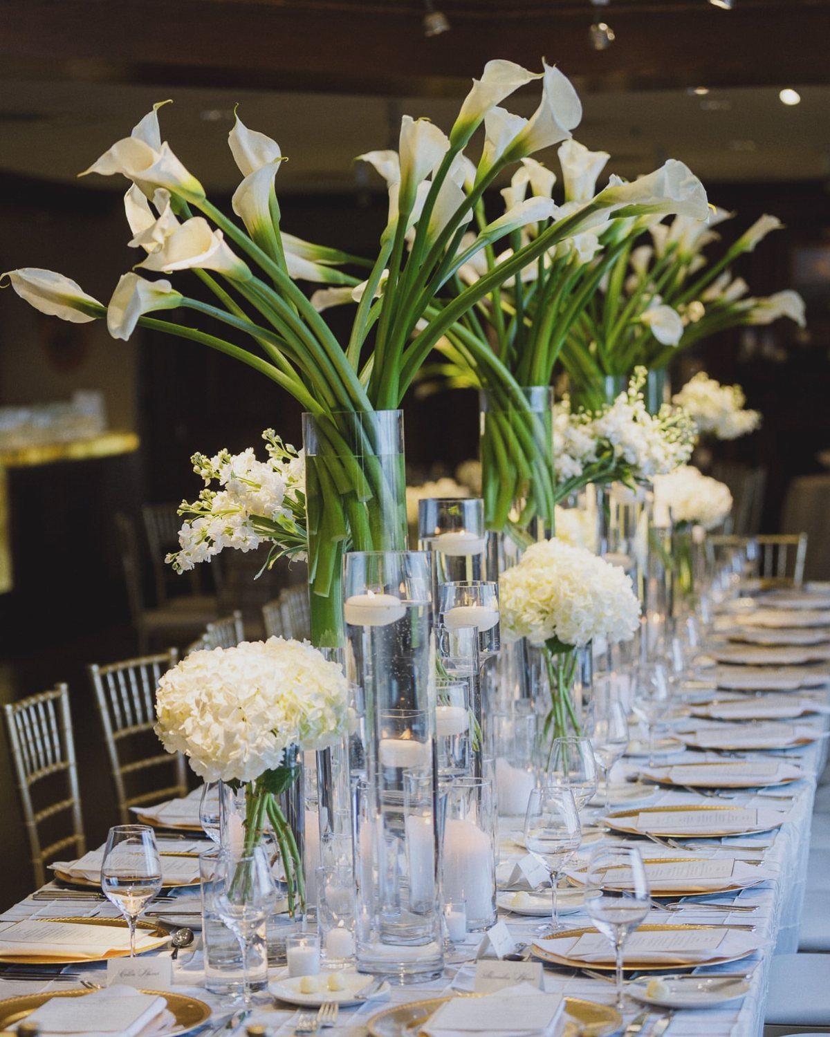 White calla lily and hydrangea centerpieces in glass vases on a wedding table.